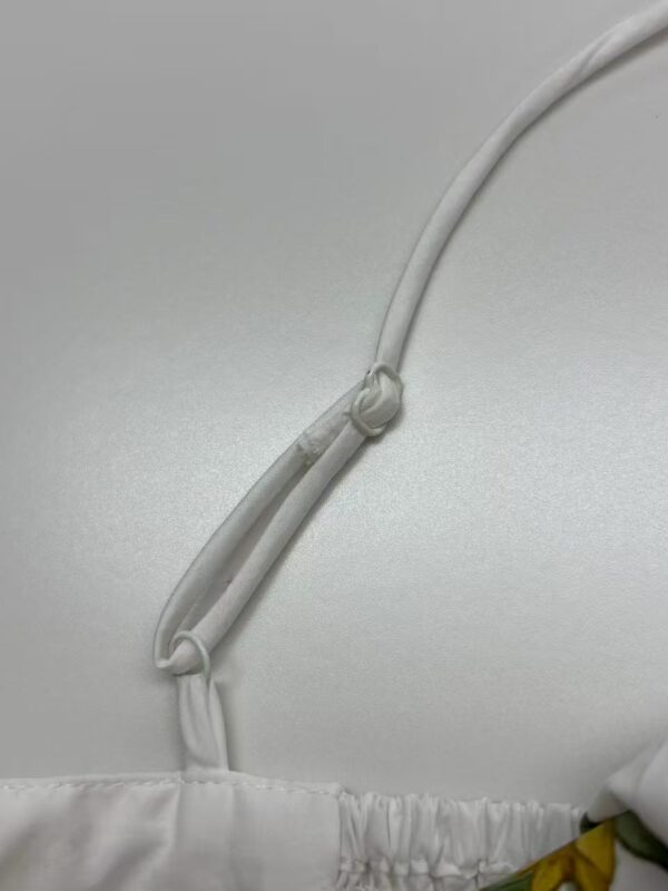 Close-up of a white adjustable strap with a knot, attached to a white fabric surface, possibly part of clothing or bedding.