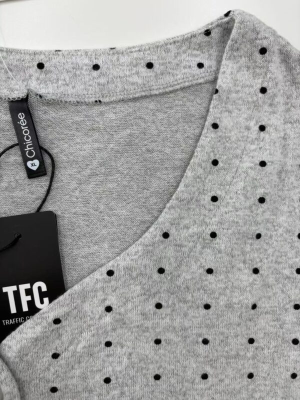 Close-up of a grey women's T-shirt with black polka dots, featuring a round neckline and a clothing tag from Chicoree, ideal for casual fashion.