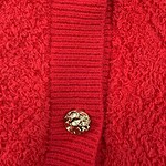 Close-up of a red wool coat featuring a textured fabric and two decorative gold buttons on a ribbed placket.