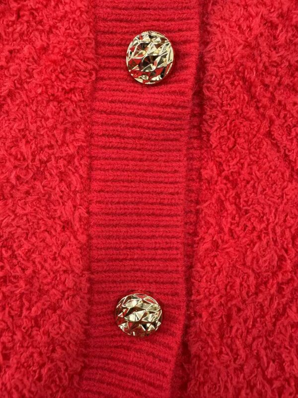 Close-up of a red wool coat featuring a textured fabric and two decorative gold buttons on a ribbed placket.
