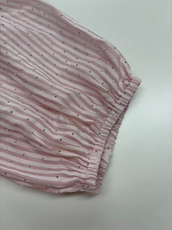 Close-up of pink fabric with white and pink stripes, decorated with small silver dots, gathered at the edge.