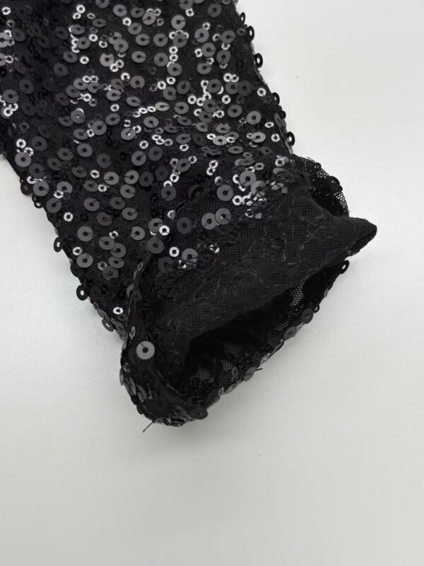 Close-up of black sequin fabric with shiny, reflective sequins on a garment, showcasing detailed craftsmanship and luxurious texture.