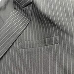 Close-up of a gray pinstripe suit jacket with a welt pocket, showcasing fine tailoring and classic design suitable for formal occasions.