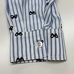 Close-up of a blue and white striped shirt with black bow patterns, featuring a buttoned cuff and detailed fabric texture.