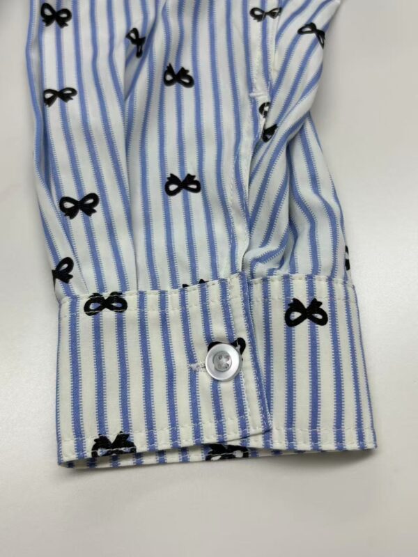 Close-up of a blue and white striped shirt with black bow patterns, featuring a buttoned cuff and detailed fabric texture.