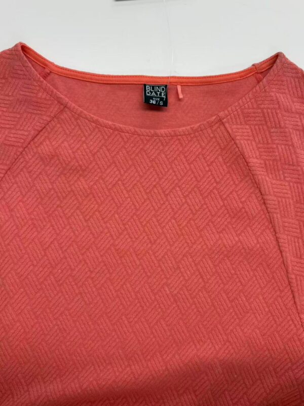 Close-up of a red textured women's blouse with a round neckline, featuring a subtle geometric pattern, suitable for casual or office wear.
