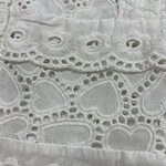 Close-up of white embroidered fabric with intricate eyelet and floral patterns, showcasing delicate craftsmanship and fine detailing.