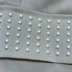 Close-up of light gray fabric with pearl embellishments, showcasing a sophisticated design element suitable for fashion and apparel.