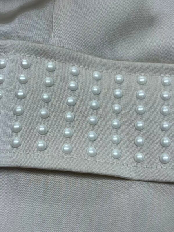 Close-up of light gray fabric with pearl embellishments, showcasing a sophisticated design element suitable for fashion and apparel.