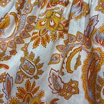 Close-up of bohemian floral print fabric with orange, yellow, and blue patterns on white background, showcasing detailed design and vibrant colors.