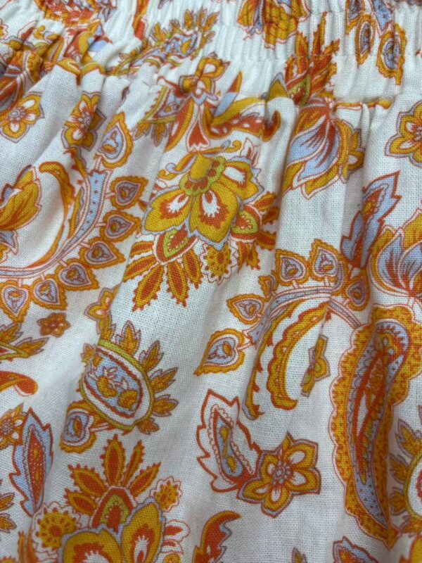Close-up of bohemian floral print fabric with orange, yellow, and blue patterns on white background, showcasing detailed design and vibrant colors.