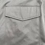 Close-up of a gray fabric pocket with flap on a garment, showcasing stitching and material texture.