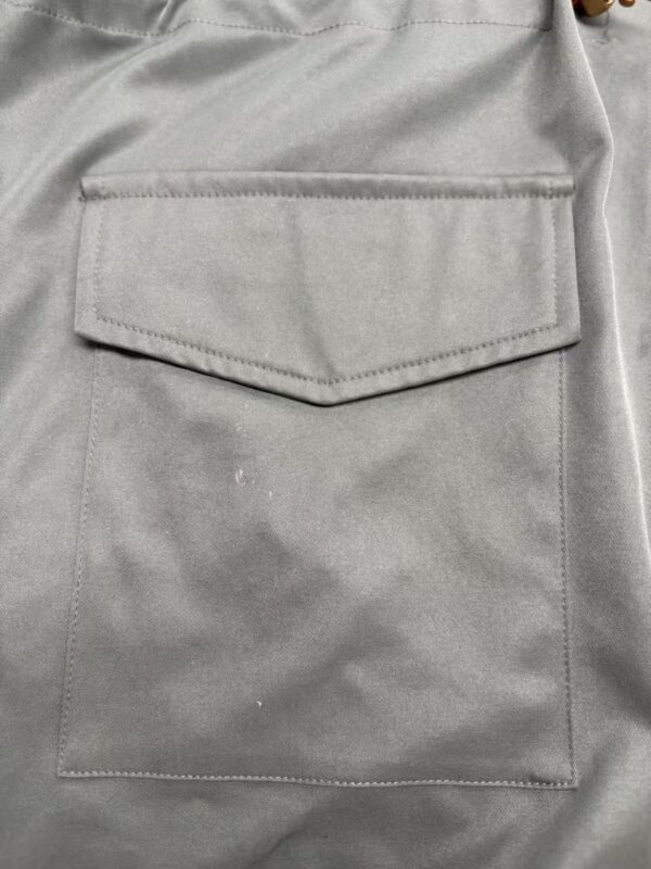 Close-up of a gray fabric pocket with flap on a garment, showcasing stitching and material texture.