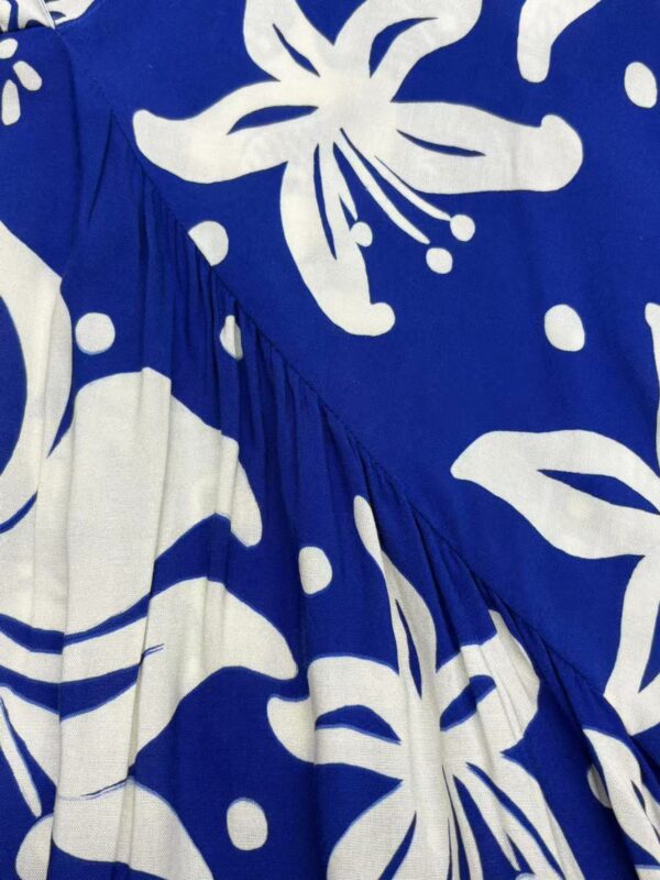 Close-up of a vibrant blue dress with large white floral patterns, featuring a gathered detail and flowing fabric, perfect for summer or casual wear.