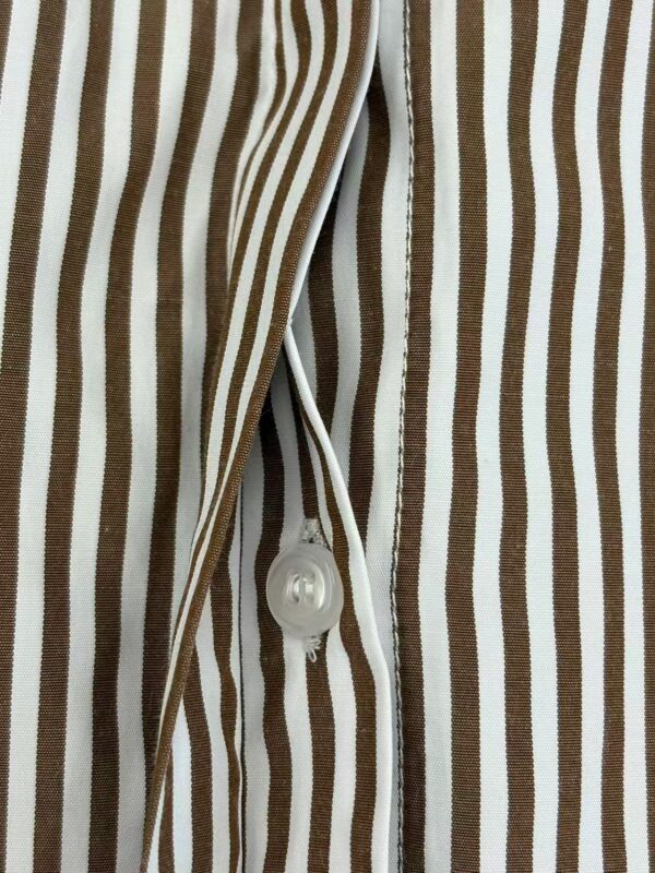 Close-up of a brown and white vertically striped shirt with a white button and zipper detail, showcasing stylish casual fashion.