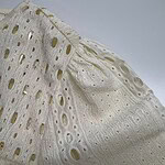 Detailed close-up of white broderie anglaise fabric showing intricate embroidery and cut-out patterns, ideal for fashion and textile design.