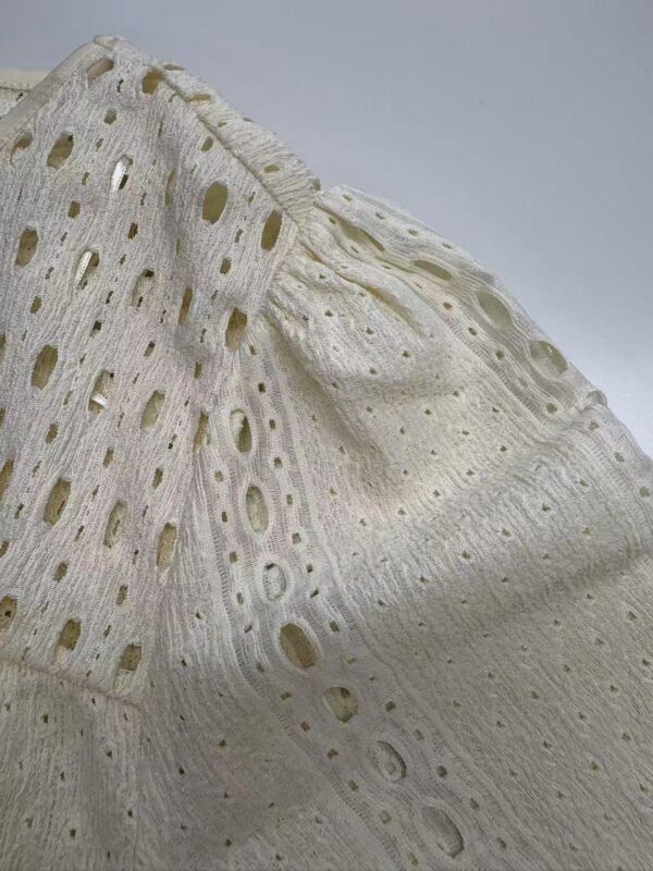 Detailed close-up of white broderie anglaise fabric showing intricate embroidery and cut-out patterns, ideal for fashion and textile design.