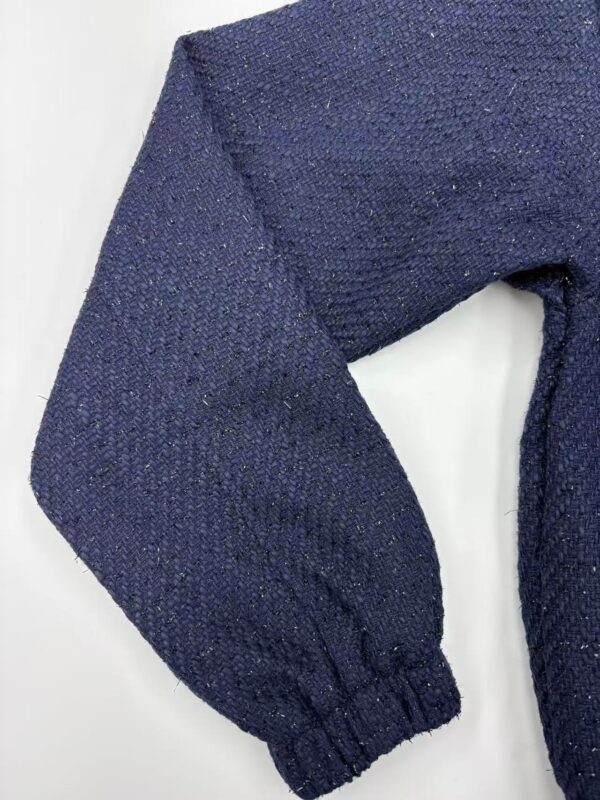 Close-up of a navy blue knitted sweater sleeve with textured fabric and elastic cuff, perfect for fall and winter fashion.