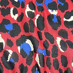 Close-up of leopard print fabric featuring black, white, and blue spots on a red background, showcasing a vibrant and stylish pattern.