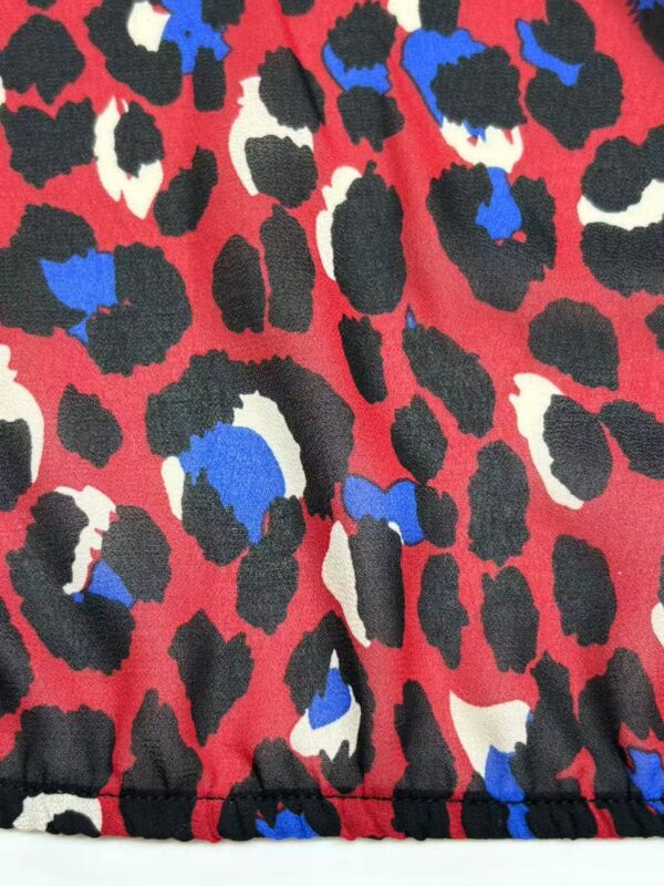 Close-up of leopard print fabric featuring black, white, and blue spots on a red background, showcasing a vibrant and stylish pattern.