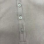 Close-up of a beige ribbed polo shirt with a collar and four buttons, showcasing a classic and stylish design suitable for casual or semi-formal wear.