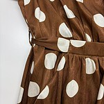 Close-up of a brown dress with large white polka dots, featuring a waist tie and ruffled sleeves, perfect for stylish casual or semi-formal occasions.