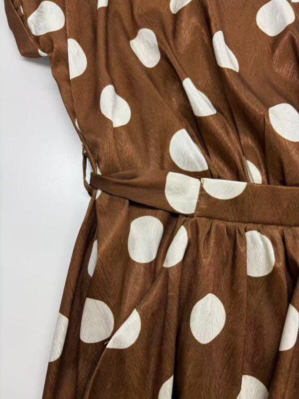 Close-up of a brown dress with large white polka dots, featuring a waist tie and ruffled sleeves, perfect for stylish casual or semi-formal occasions.