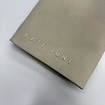 Beige Kate June fashion packaging bag with embossed logo on smooth textured surface, minimalistic design, ideal for luxury clothing or accessories branding.