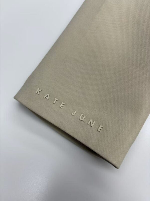 Beige Kate June fashion packaging bag with embossed logo on smooth textured surface, minimalistic design, ideal for luxury clothing or accessories branding.