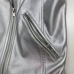 Close-up of a silver leather jacket featuring a diagonal zippered pocket, showcasing modern fashion and high-quality material.