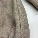 Close-up of a beige woolen coat showing detailed fabric texture and seam, highlighting quality craftsmanship and material.