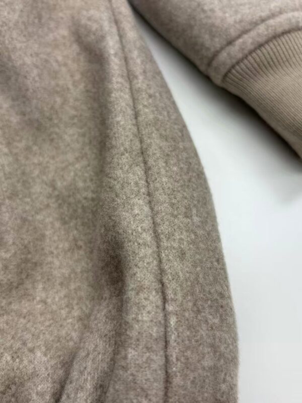Close-up of a beige woolen coat showing detailed fabric texture and seam, highlighting quality craftsmanship and material.