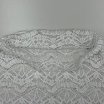 Close-up of intricate white lace fabric with floral and geometric patterns, ideal for fashion and dressmaking.