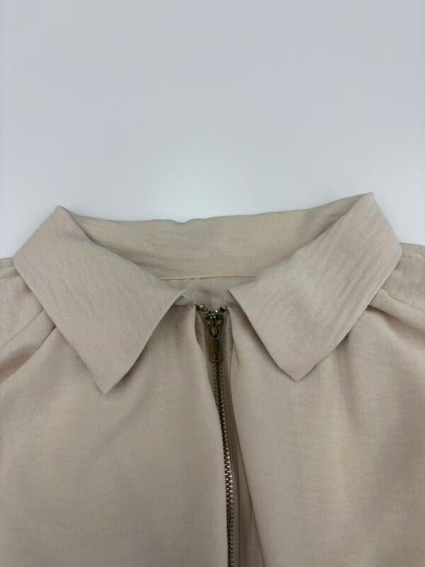 Close-up of a beige women's jacket with a collar and zipper, showcasing a stylish and casual fashion piece.