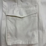 Close-up of white cargo pants featuring a large front pocket with flap closure, made from durable fabric, suitable for casual or workwear styles.