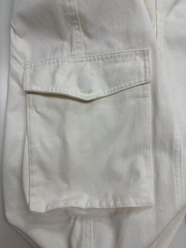 Close-up of white cargo pants featuring a large front pocket with flap closure, made from durable fabric, suitable for casual or workwear styles.