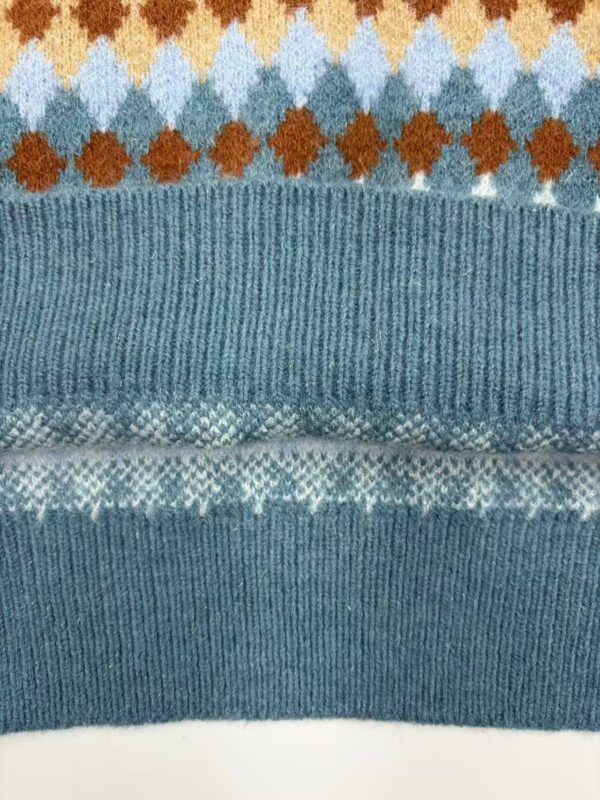 Close-up of a knitted sweater with geometric patterns in blue, orange, and white, showcasing detailed knitting and vibrant colors.