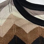 Close-up of a stylish knit sweater featuring a geometric pattern in beige, brown, black, and cream with a black ribbed neckline.
