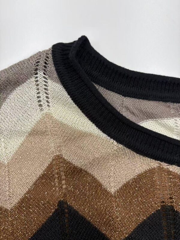 Close-up of a stylish knit sweater featuring a geometric pattern in beige, brown, black, and cream with a black ribbed neckline.