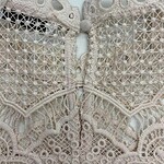 Close-up of intricate beige lace fabric with detailed embroidery and cut-out patterns, suitable for fashion and bridal wear.