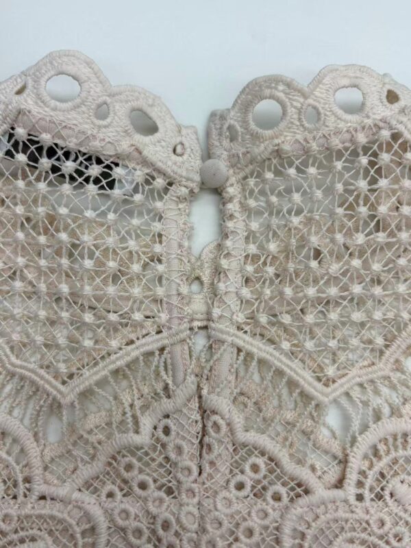 Close-up of intricate beige lace fabric with detailed embroidery and cut-out patterns, suitable for fashion and bridal wear.
