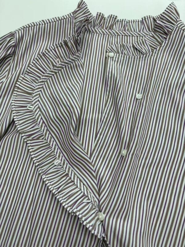 Close-up of a stylish women's blouse with vertical black and white stripes, ruffled collar, and button-down front, perfect for casual or office wear.