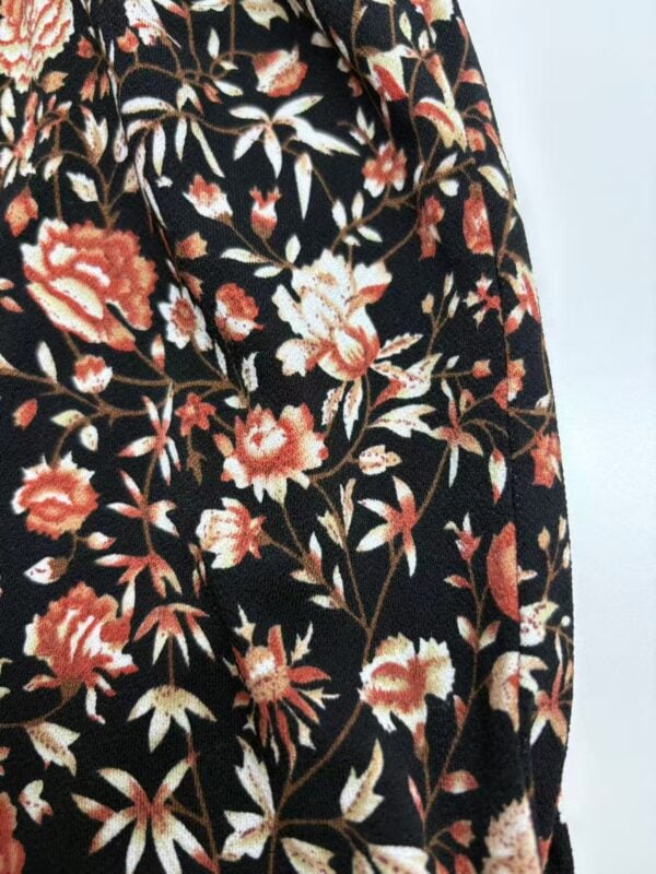 Close-up of fabric with a floral pattern featuring red, white, and beige flowers on a black background, ideal for fashion and clothing design.