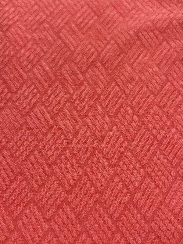 Close-up of red textured fabric with a geometric pattern, suitable for fashion or upholstery design.