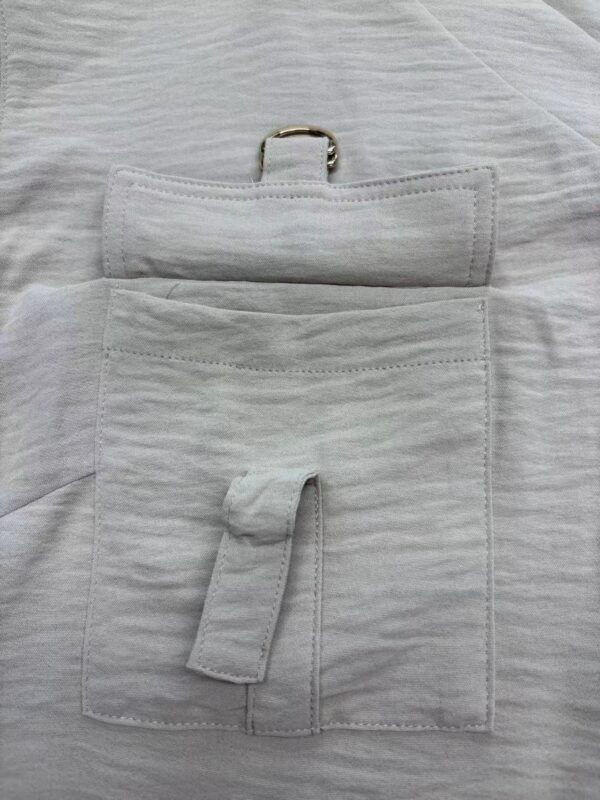 Close-up of a white medical pouch with a pocket, strap, and metal ring, placed on a white fabric surface, used for organizing medical tools.