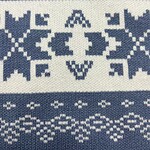 Close-up of a winter knit sweater featuring traditional Nordic patterns in white on a blue background, showcasing detailed geometric designs.