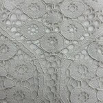 Close-up of intricate white lace fabric with floral and geometric patterns, ideal for fashion and bridal wear.