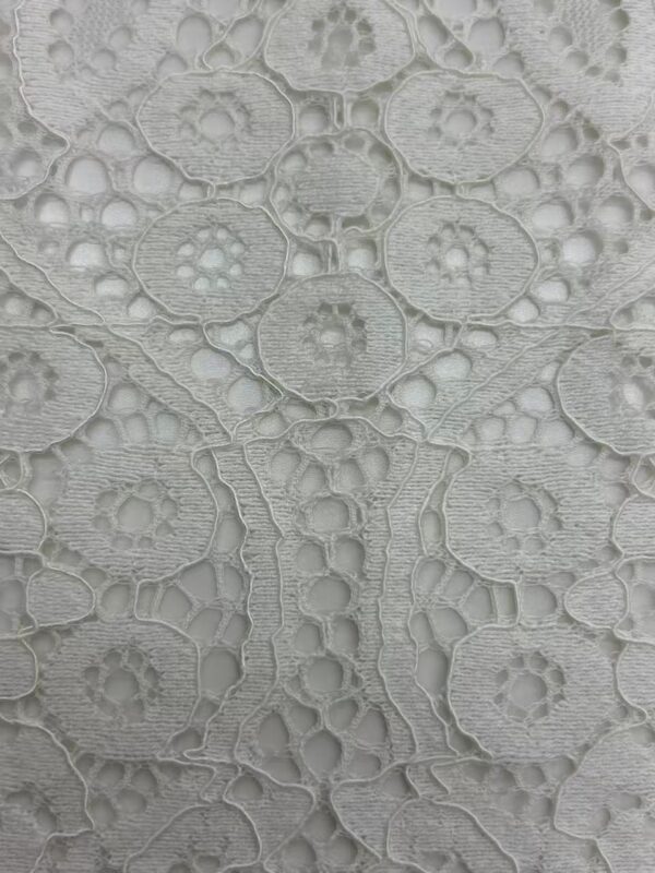 Close-up of intricate white lace fabric with floral and geometric patterns, ideal for fashion and bridal wear.