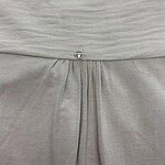 Close-up of light gray dress fabric with a small decorative button and pleats, showcasing high-quality material and craftsmanship.