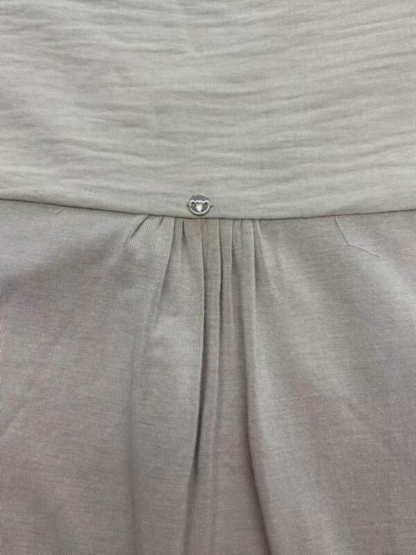 Close-up of light gray dress fabric with a small decorative button and pleats, showcasing high-quality material and craftsmanship.